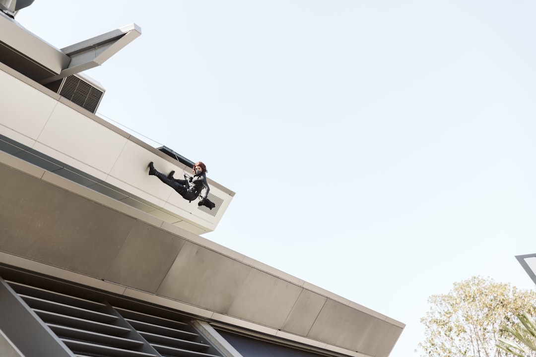 Roof Maintenance Technician man in black jacket and black pants sitting on white concrete building during daytime