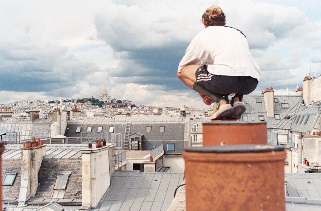 man in white t-shirt and black pants sitting on brown concrete building during daytime