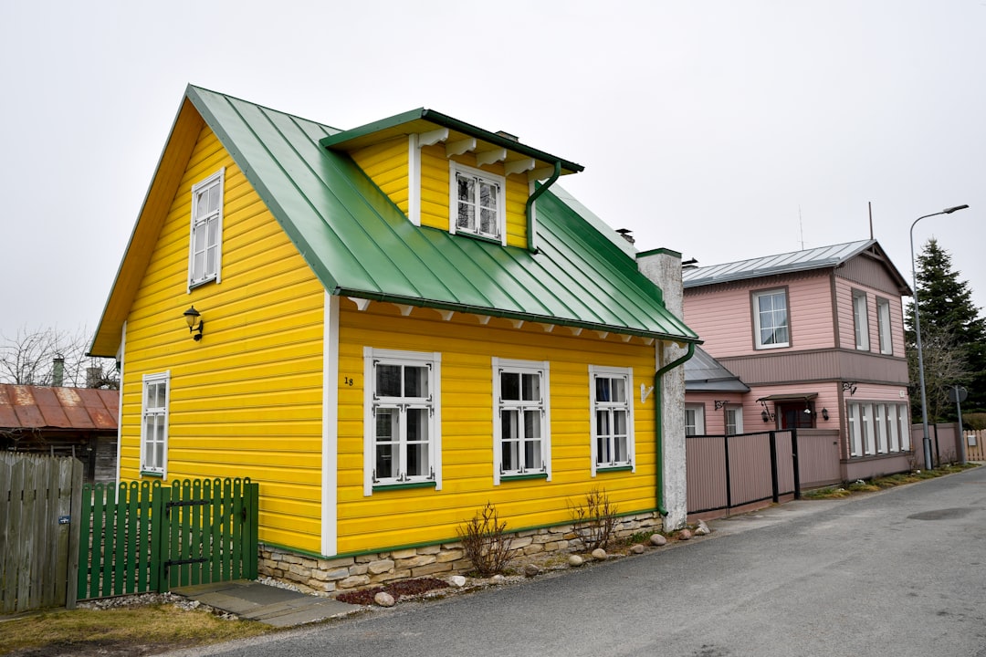 Charming yellow house with a green roof by a street.