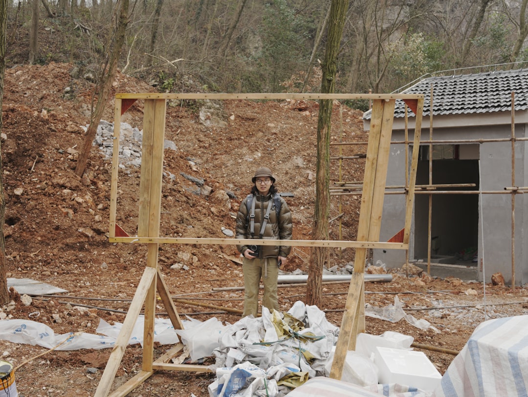 Person stands behind wooden frame at construction site.