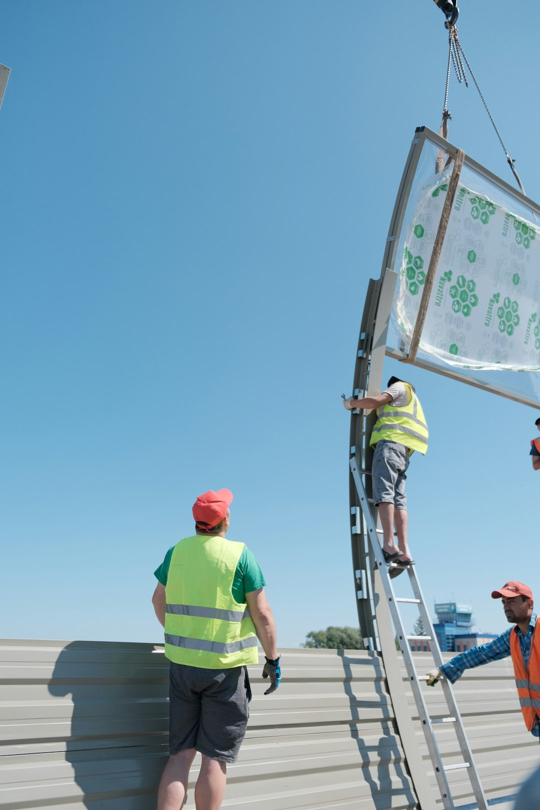 Workers are installing a large panel under a clear sky.