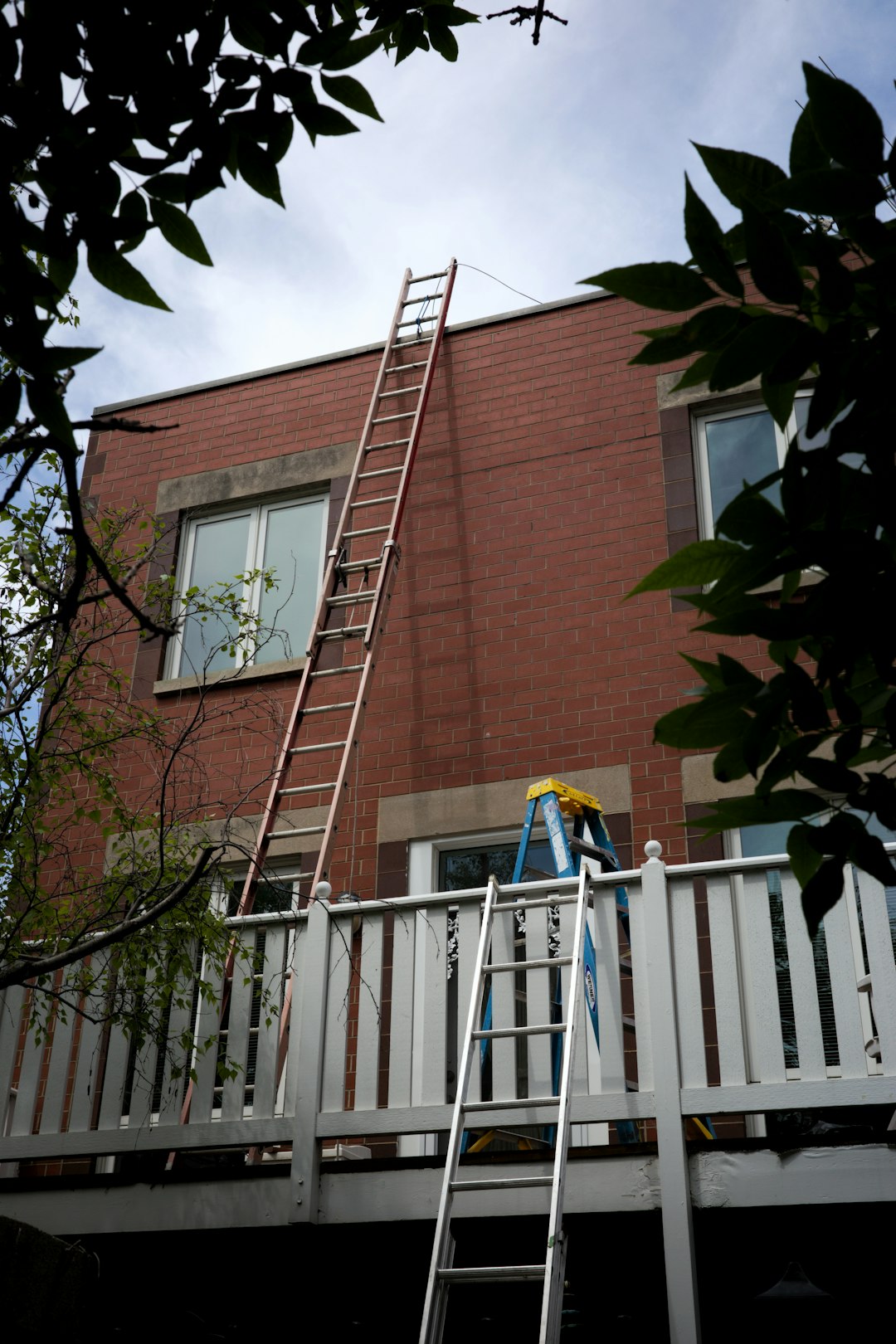 Roof Work Preparation Ladders leaning against a brick building with a balcony.
