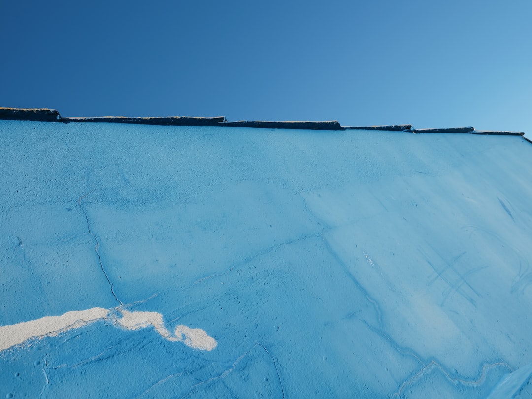 Bright blue stucco wall with cracks and coping stones against a clear blue sky