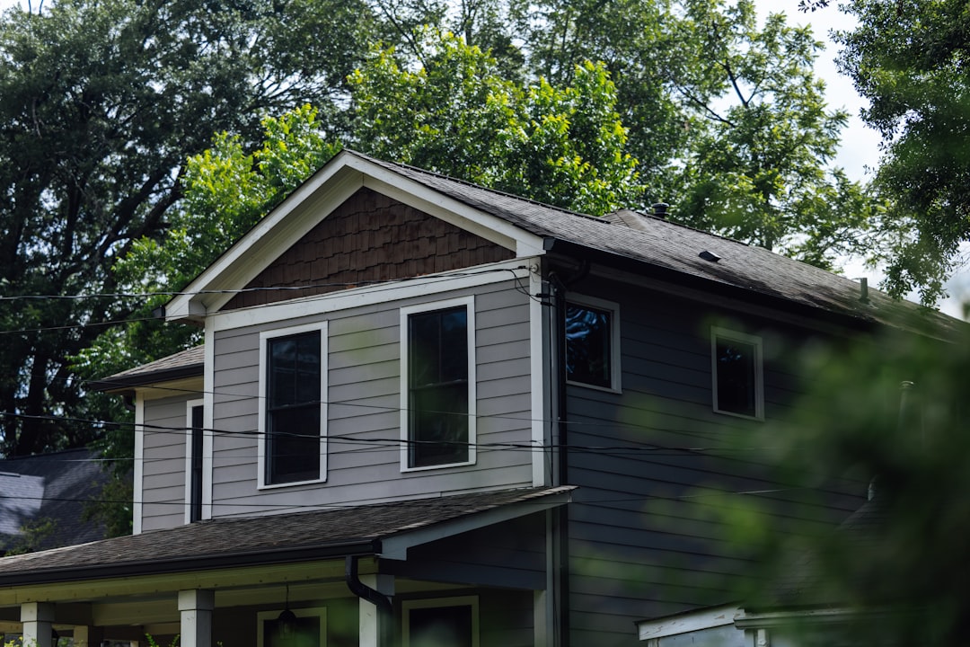 Gray house with multiple windows surrounded by green trees.