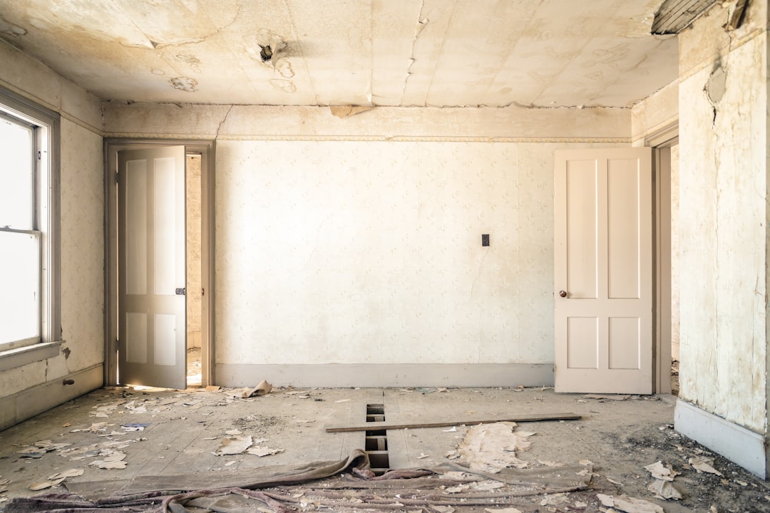 An abandoned room with peeling wallpaper, two open doors, and a damaged wooden floor