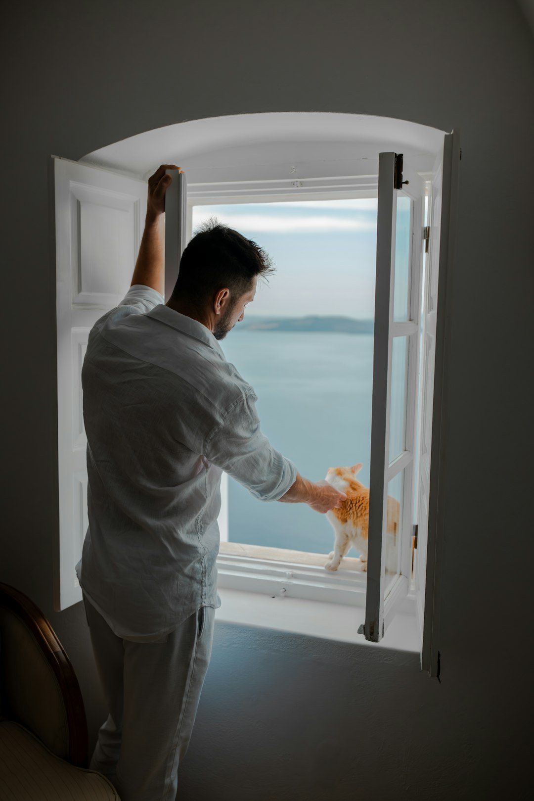 Man interacts with cat on windowsill overlooking the ocean.