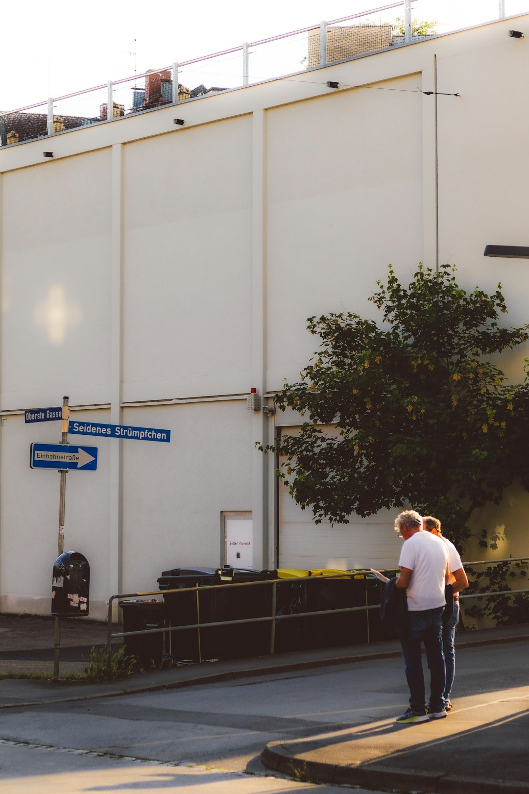 Two men stand near a building, looking at something.