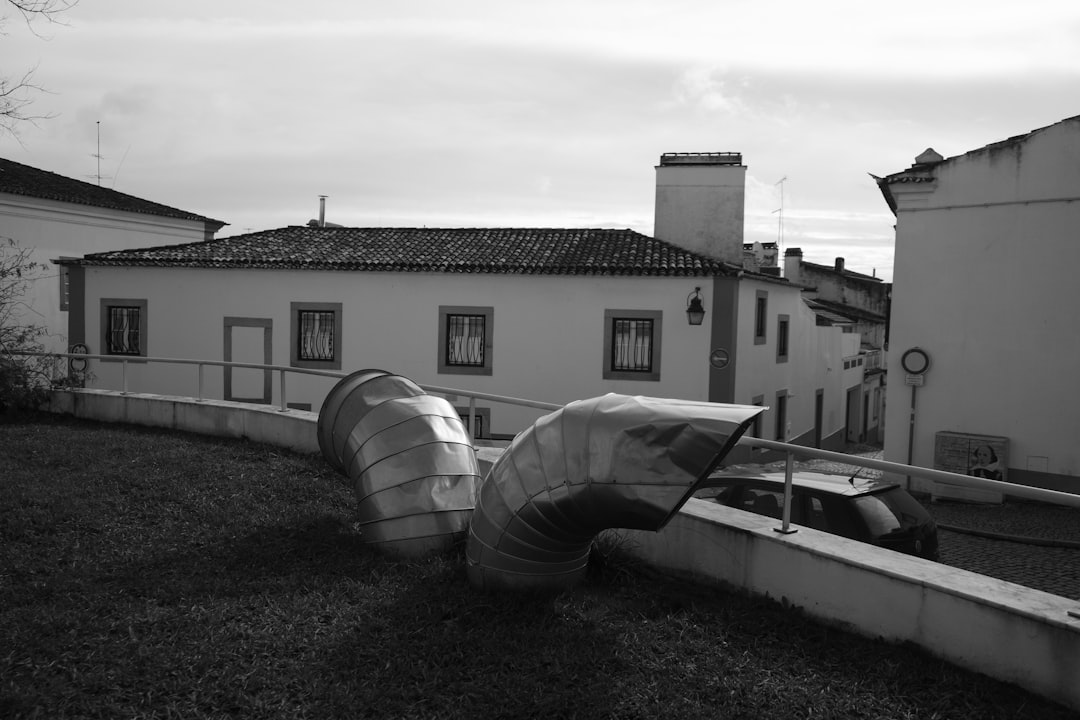 28085261dbdc4b5baca3b10b3e81a59f Curved metal pipes on grassy slope near buildings