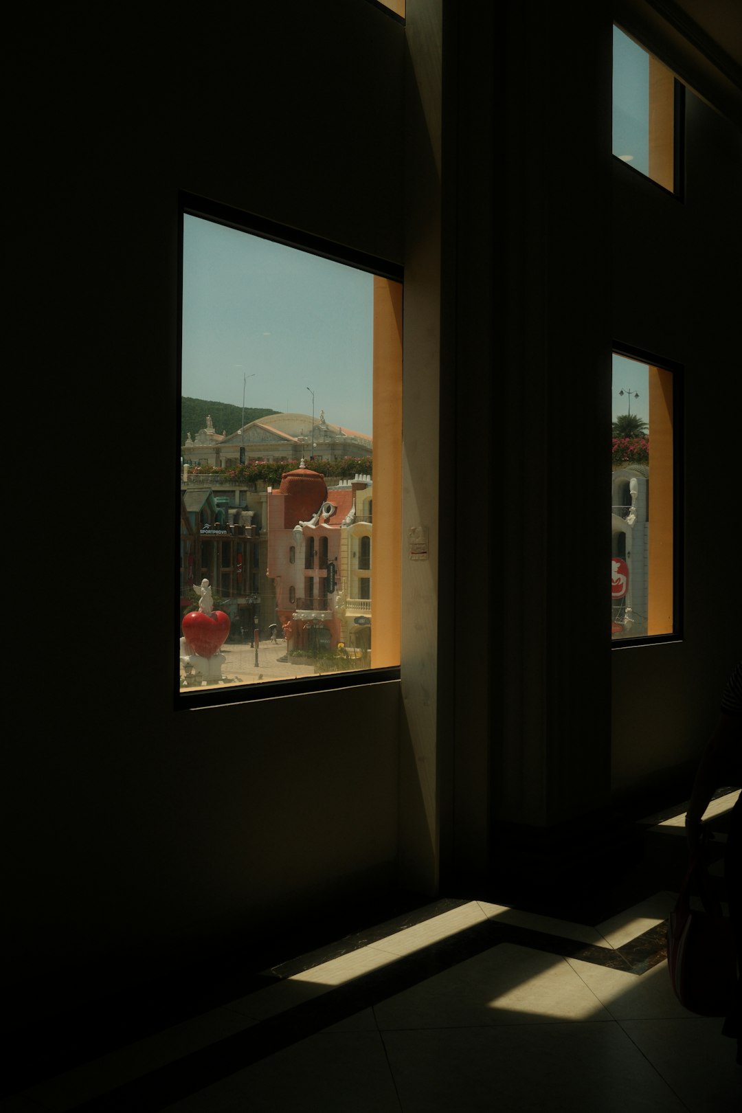 Dark interior with windows overlooking a vibrant, sunny town.