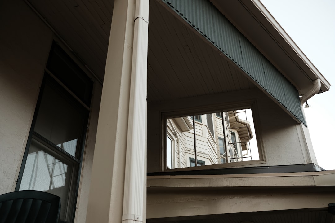 Gutter installation on a beige building with a downspout and blue-green trim