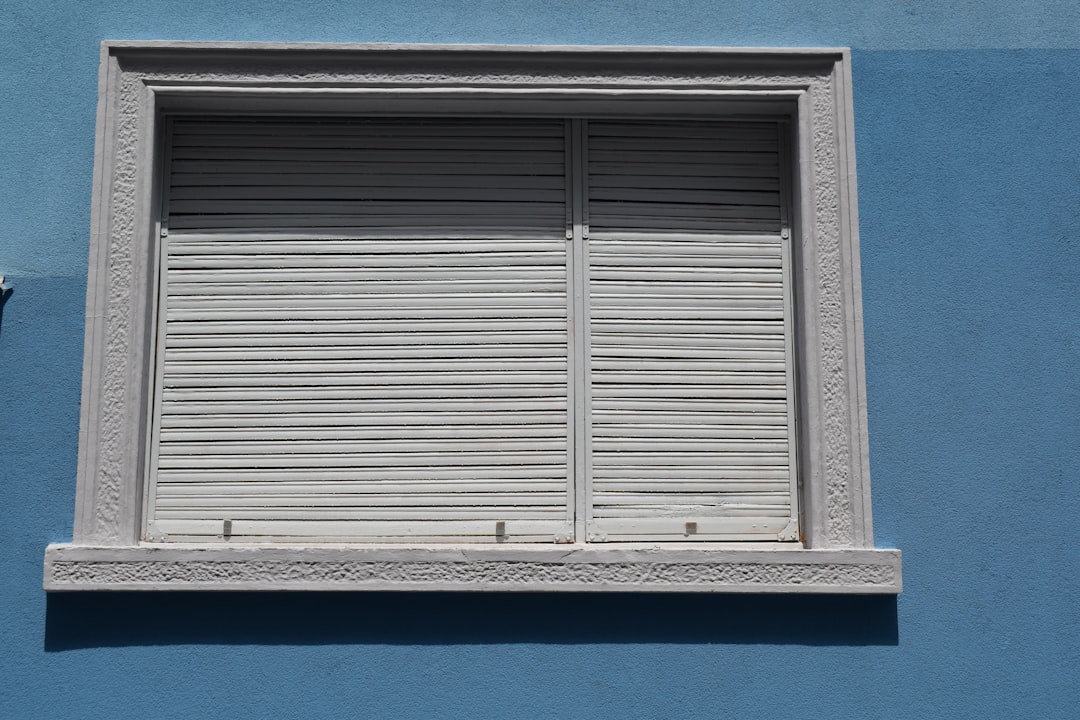 5909b21e62e047a5bd70dbfe1d2de307 A white window with closed shutters on a blue wall