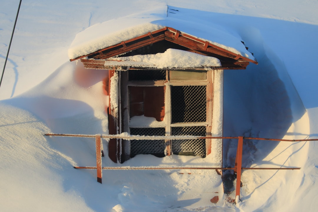 a small house covered in snow next to a fence