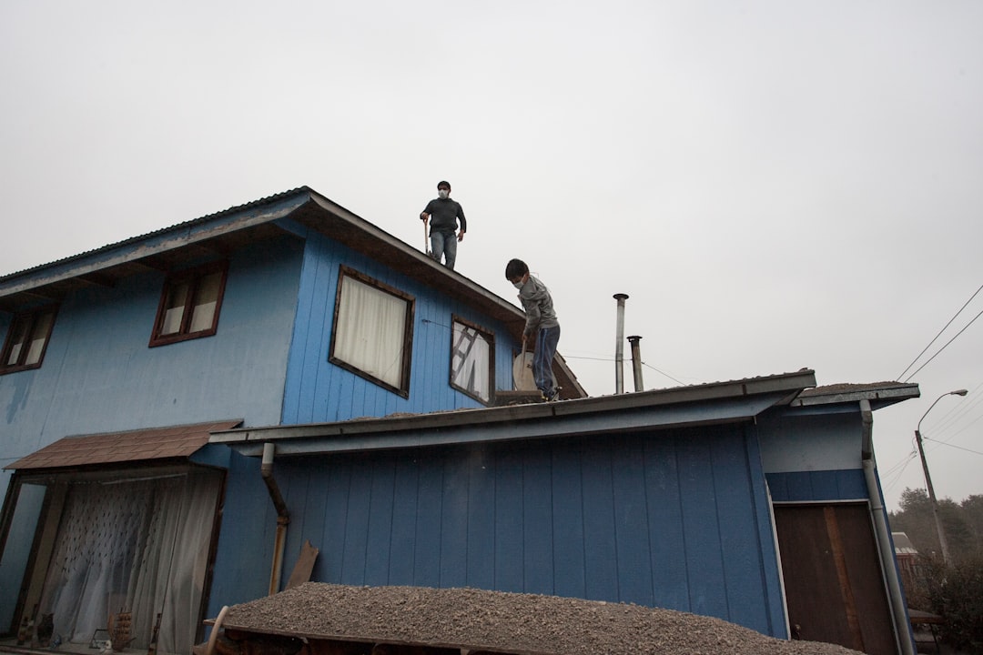 Two men working on the roof of a blue house.