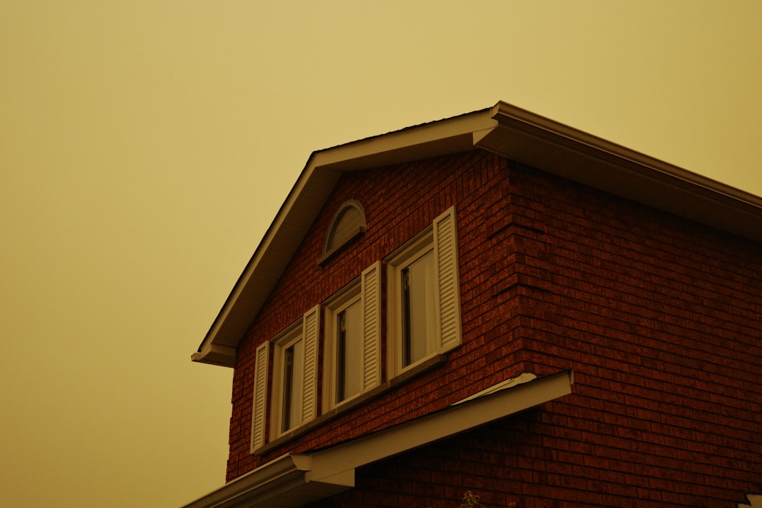 70d9074067f84184a0dc00498e3e6758 Red brick house with white windows against a yellow sky.