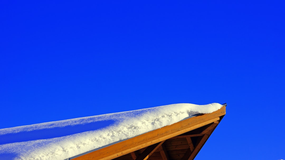 Snow rests on a wooden roof against a blue sky.