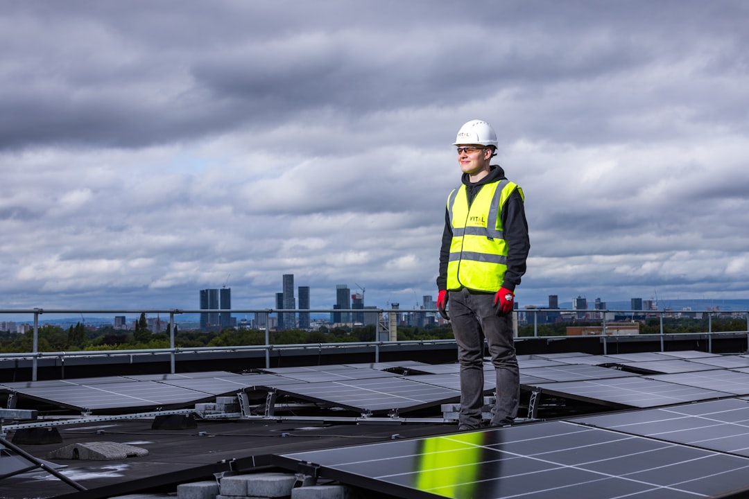 9397f3d91ea3455ca447f95dfe0d2723 a man standing on top of a roof next to solar panels