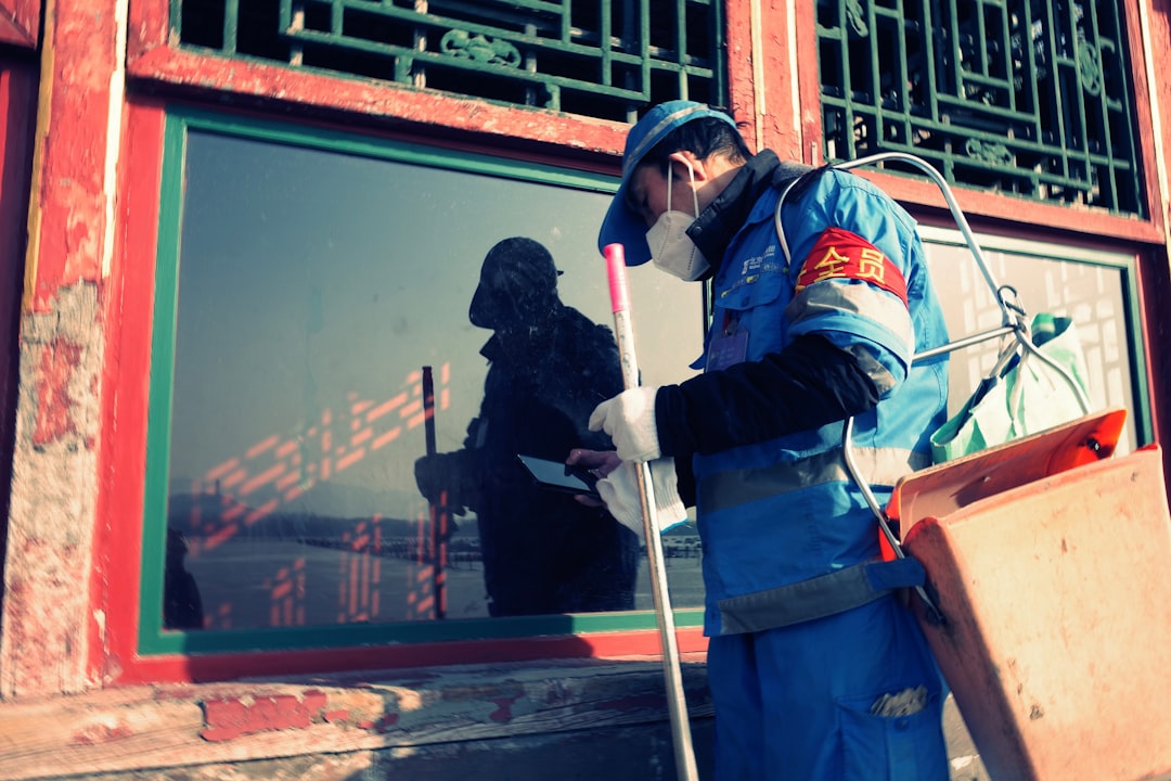 96931db71ff44127b1311b8135f987bf Worker in blue uniform cleans window with spray bottle