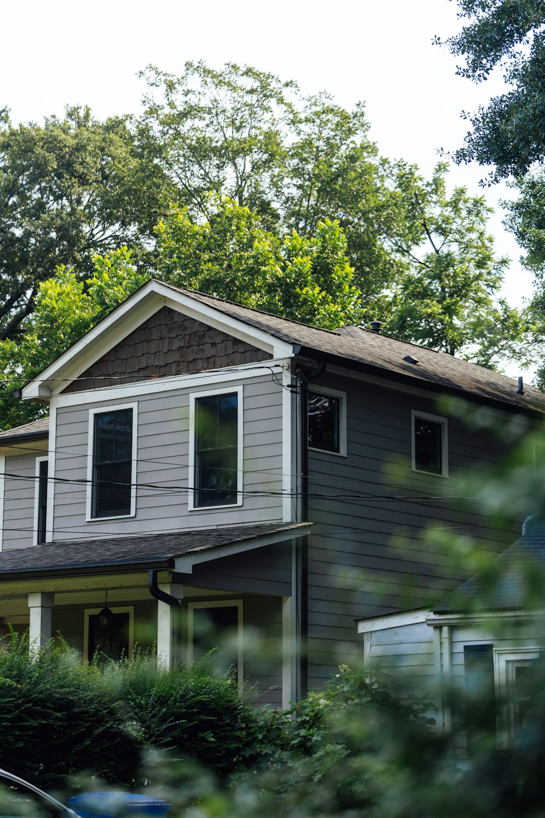 9d10d7457c4b4da7991c2520e00cc34a A gray two-story house surrounded by green trees.