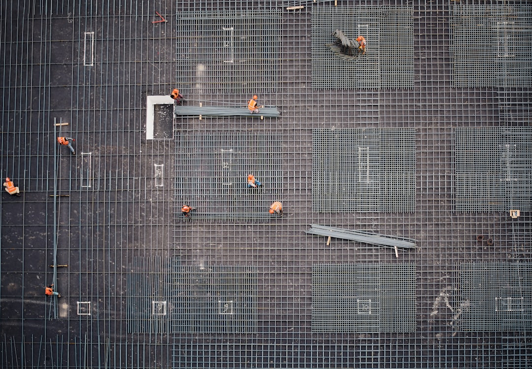 Workers in orange vests placing steel rebar on a construction site grid