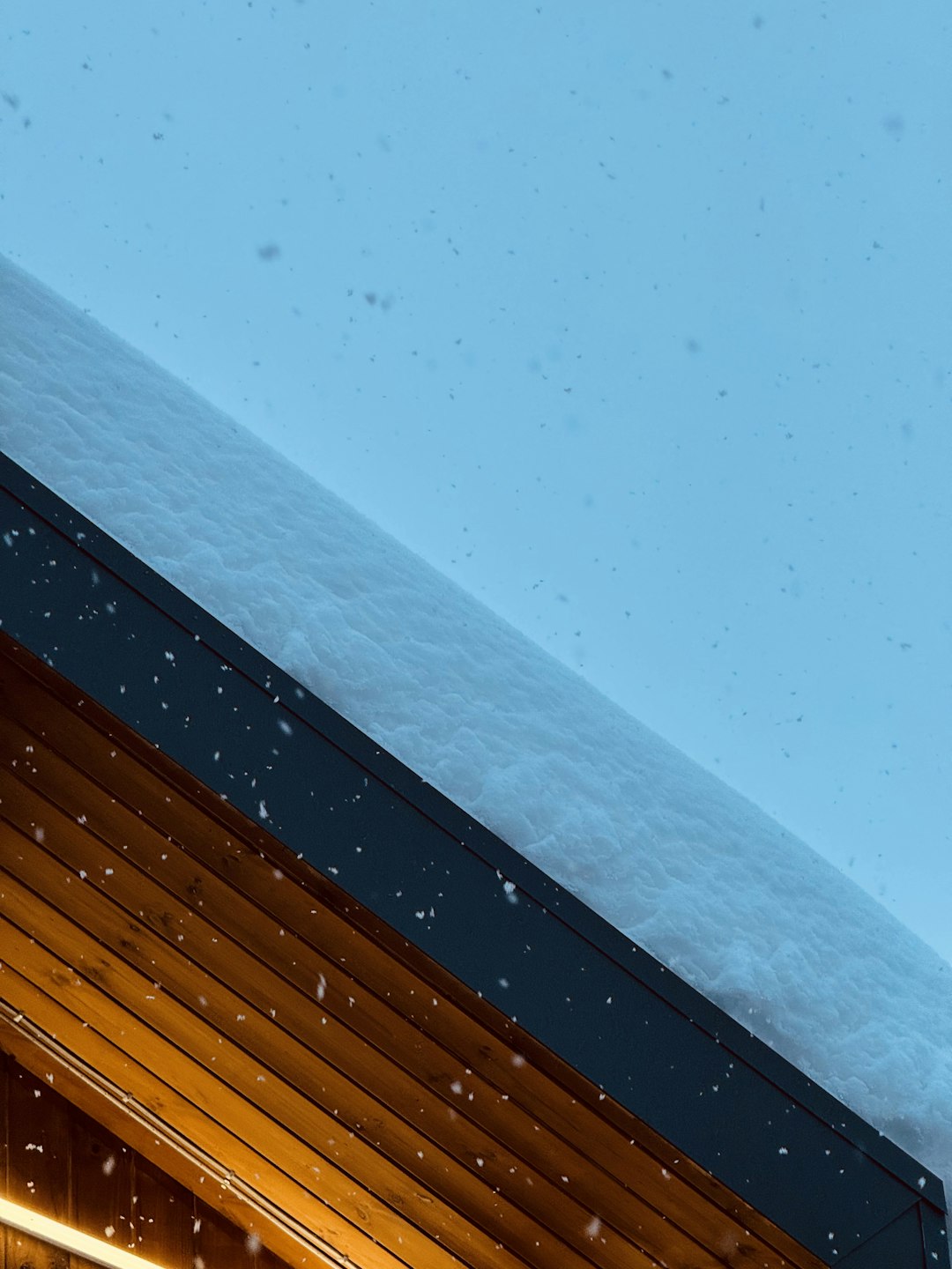 Snow falling on a wooden roof at dusk.