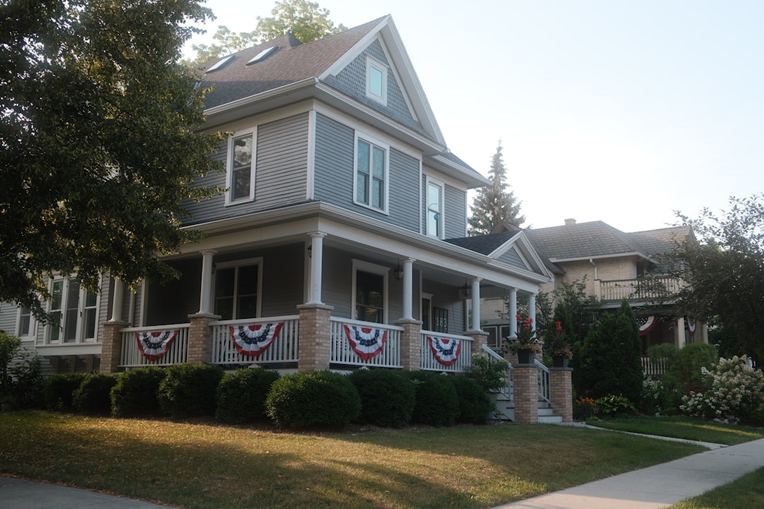 af7c9b3443c948fb8ae13f93d19bc49f A gray two-story house with a porch and patriotic bunting.