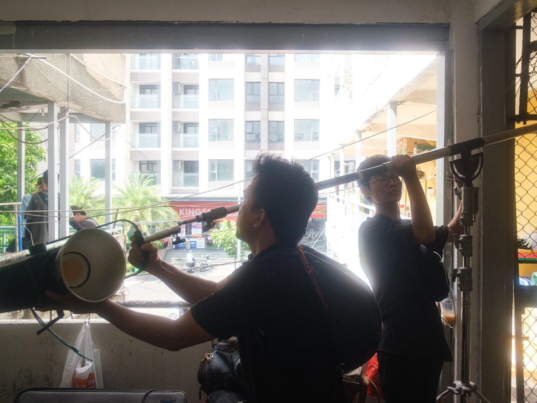 af8db588dc2d41e29f7909fd945bb980 Two technicians adjust film production equipment near a window.