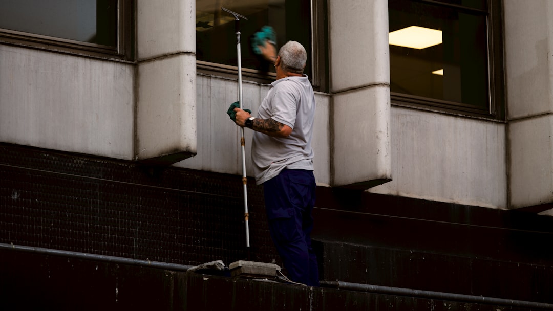 A person cleaning a window with a long squeegee on a building exterior