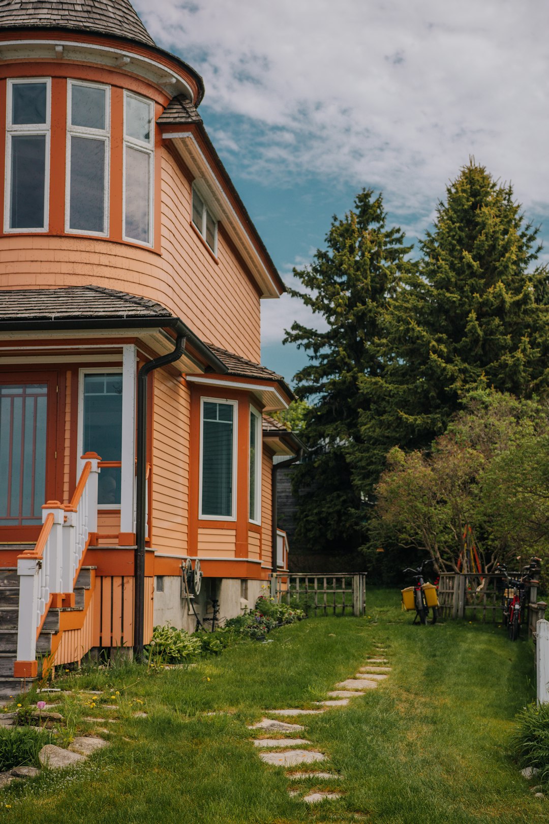 Orange house with white stairs, green lawn, and tall trees.
