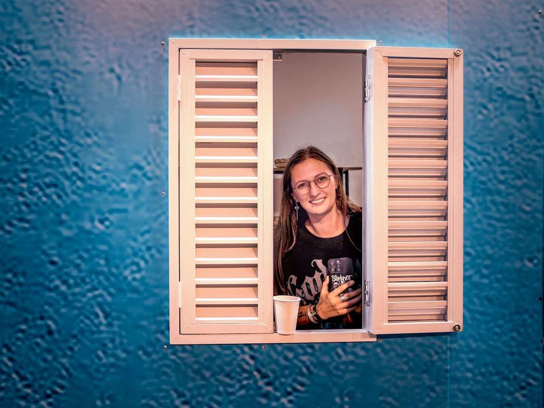 Young woman smiles from a window with shutters