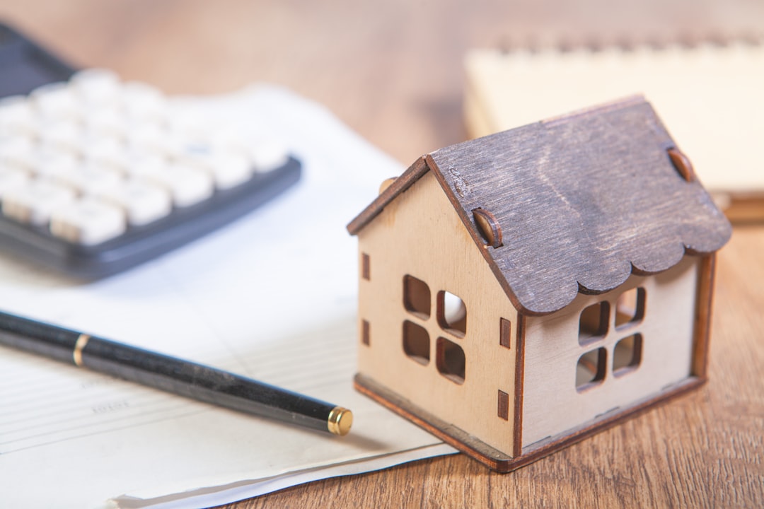 c612d94cd2684c24b9a790184645f7fd Model house with calculator and pen on desk.