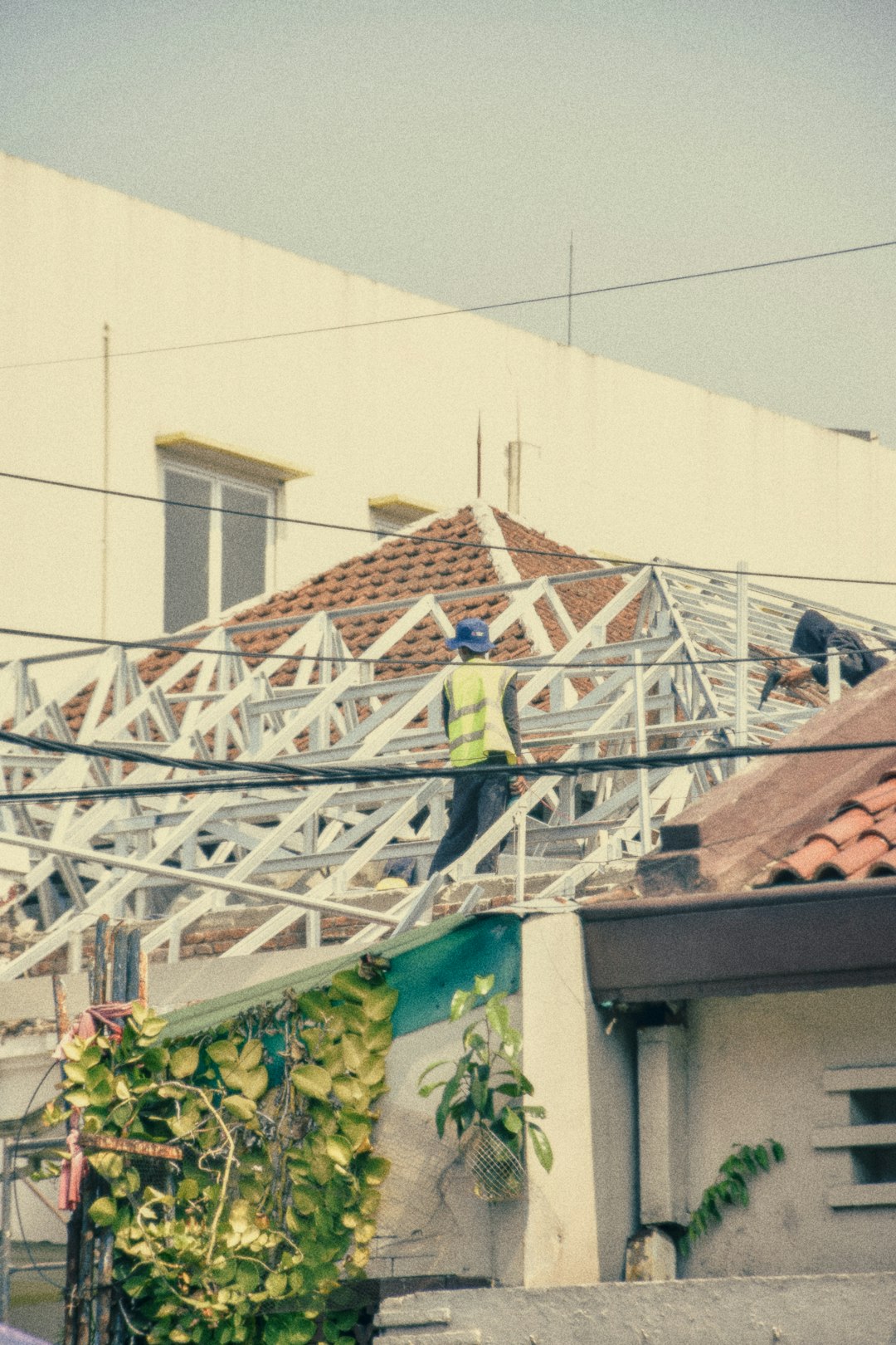 d73fd6a31b3a4ec6add8091d68f8cf18 A person in a high-visibility vest working on a metal roof frame.