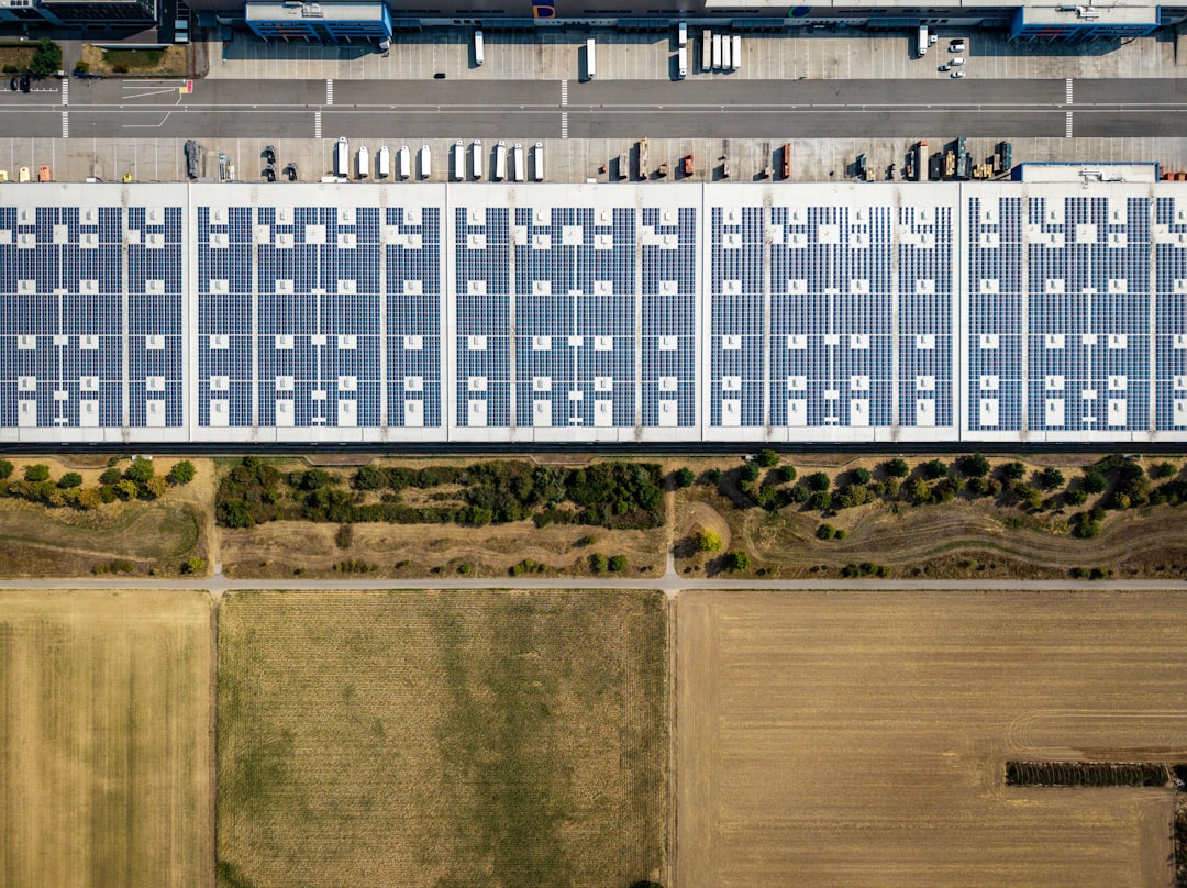 An aerial view of a large warehouse roof covered in solar panels beside fields