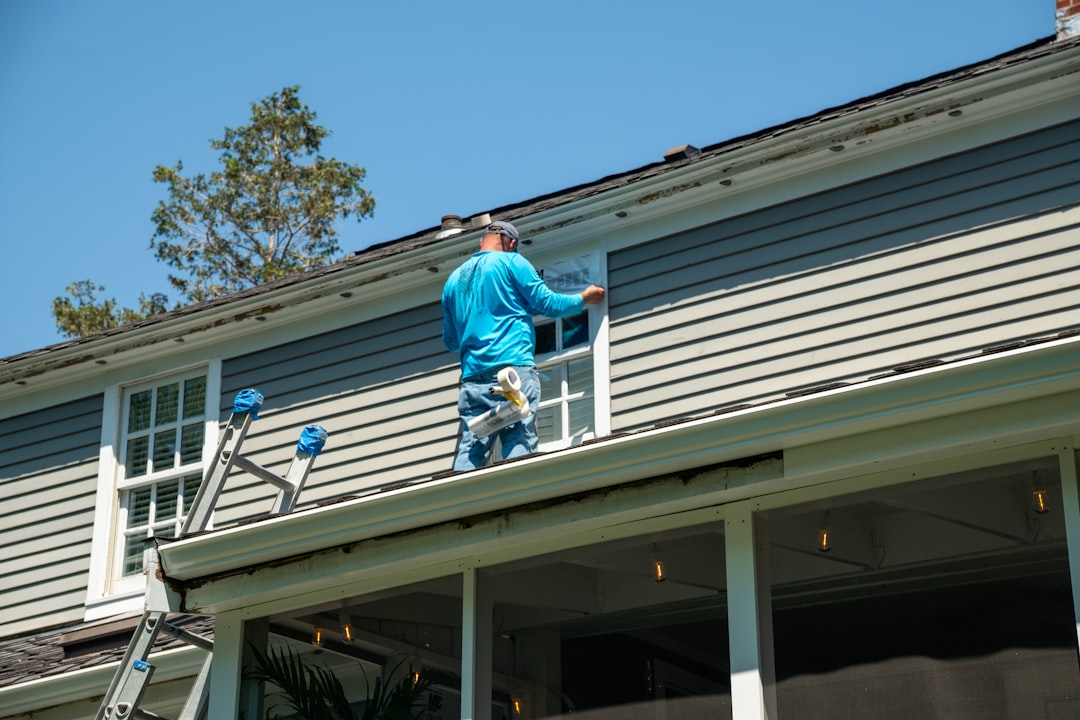 A person in a blue shirt applying tape to a window on a house roof.