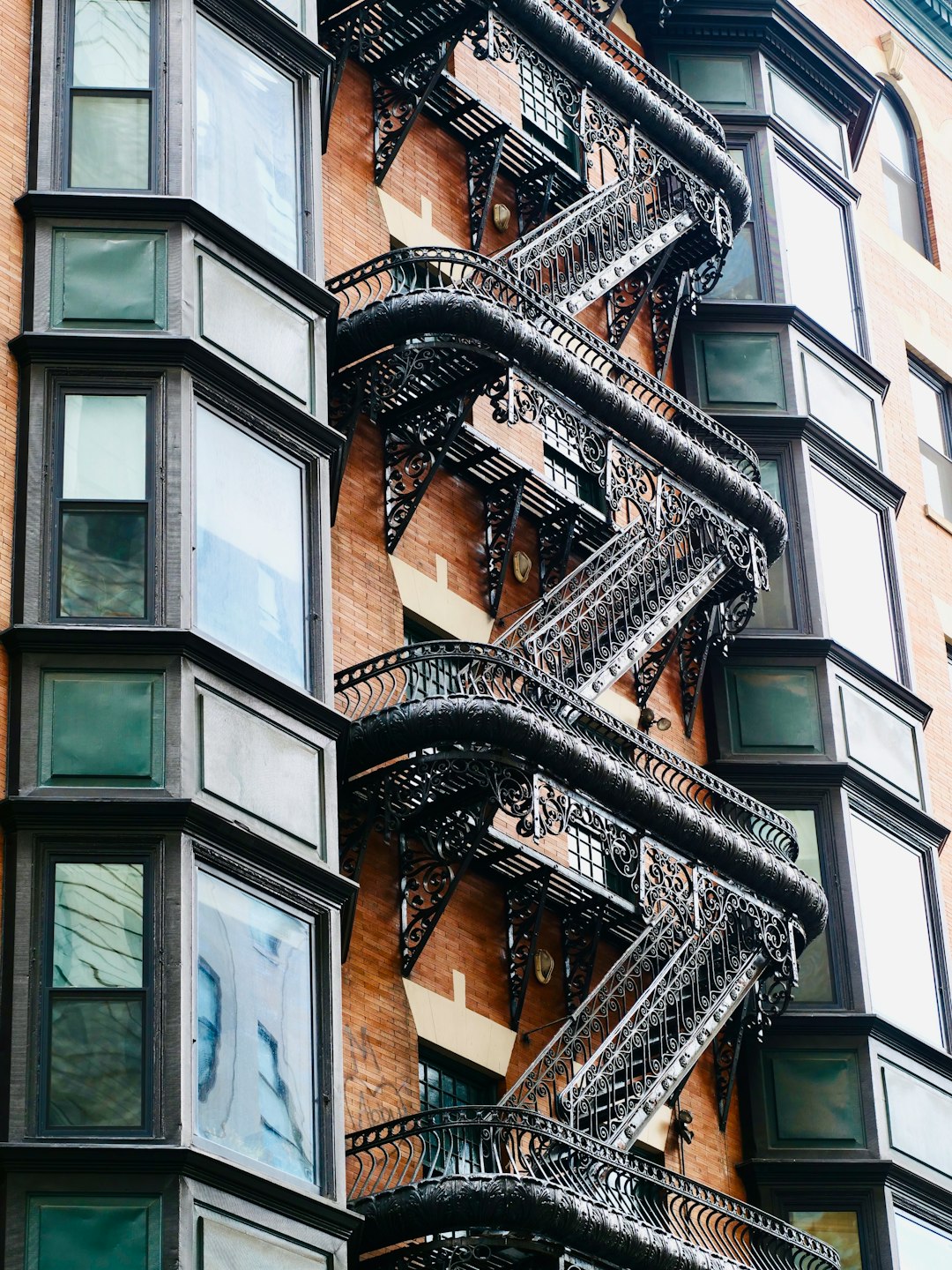 ea57d9fdaa00404f87fd9ef36e0beeeb A brick building with black fire escapes and bay windows