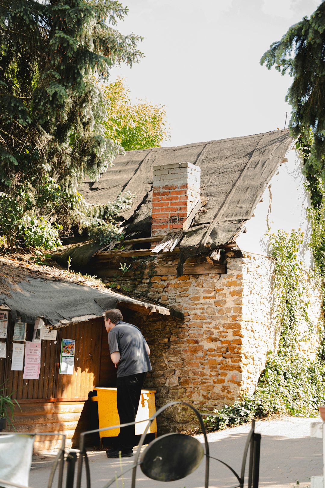ef8e06211d8645cb8b018863be29d860 Man looking at notice board beside old brick building.