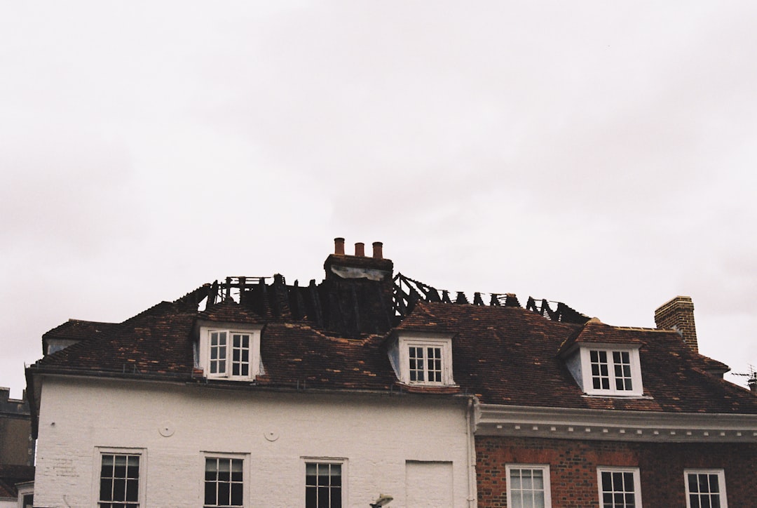 A building with a damaged roof and charred wooden beams under a cloudy sky