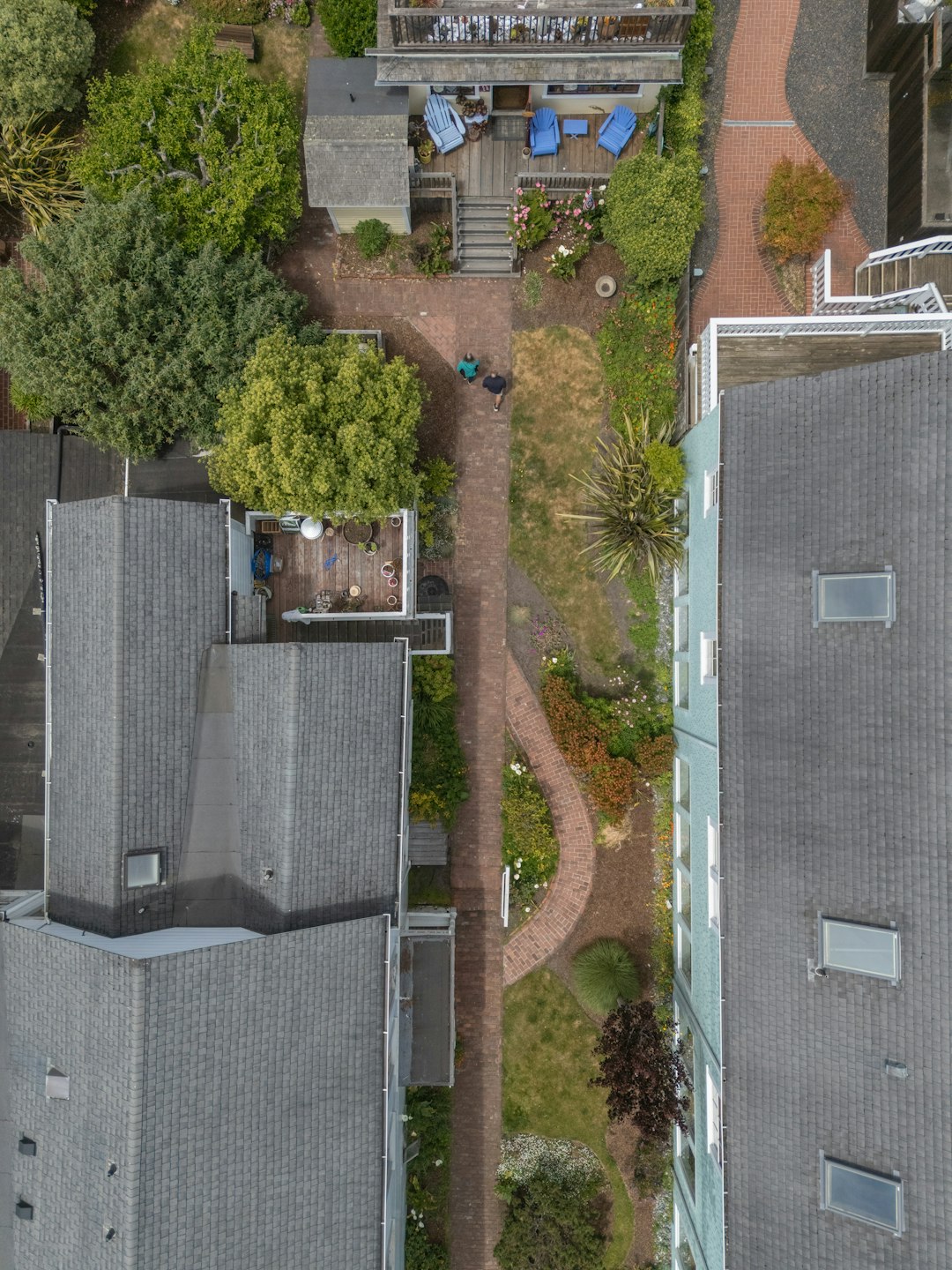 Residential buildings flank a winding brick path and green garden.