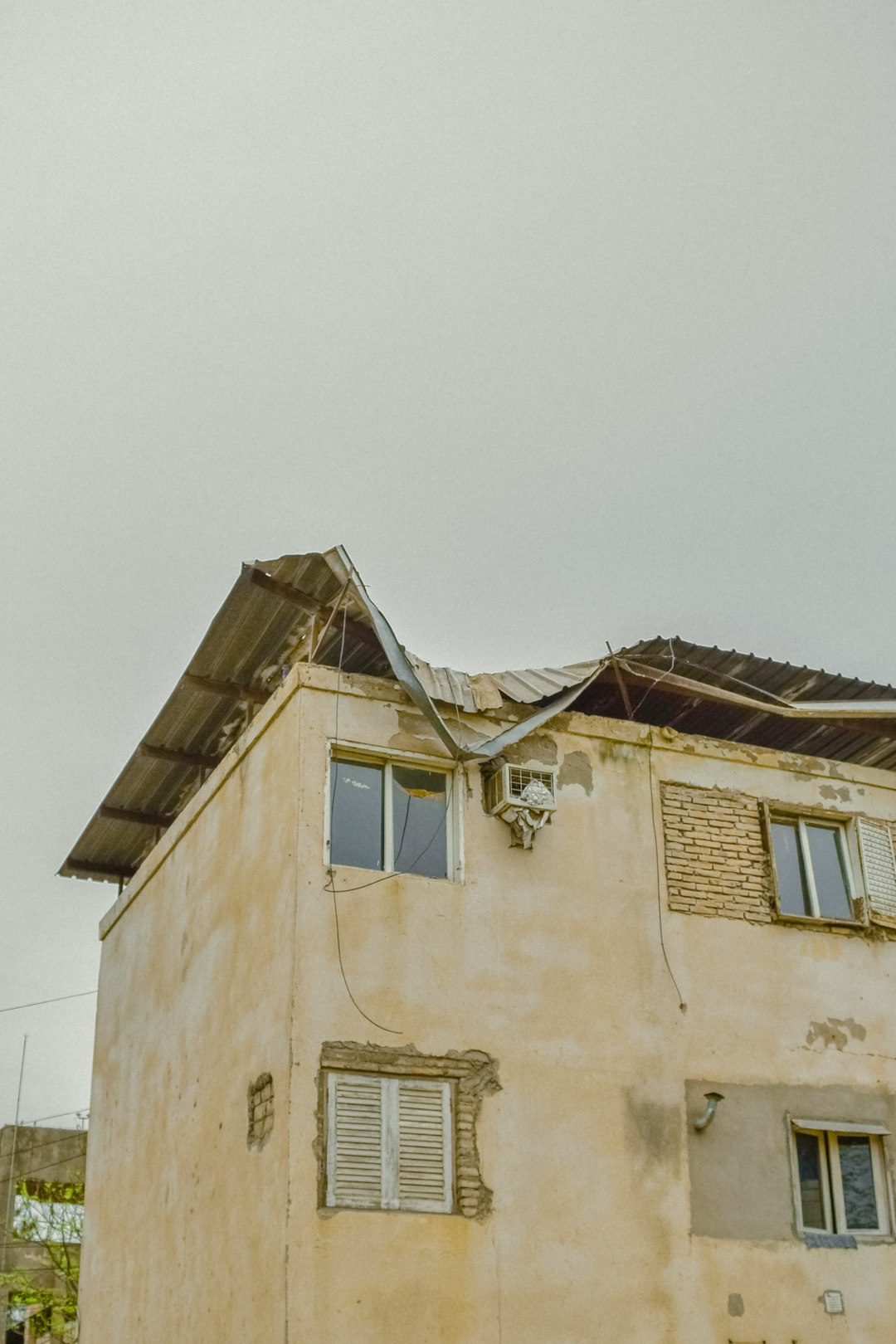 A damaged building with a collapsed metal roof under a grey overcast sky