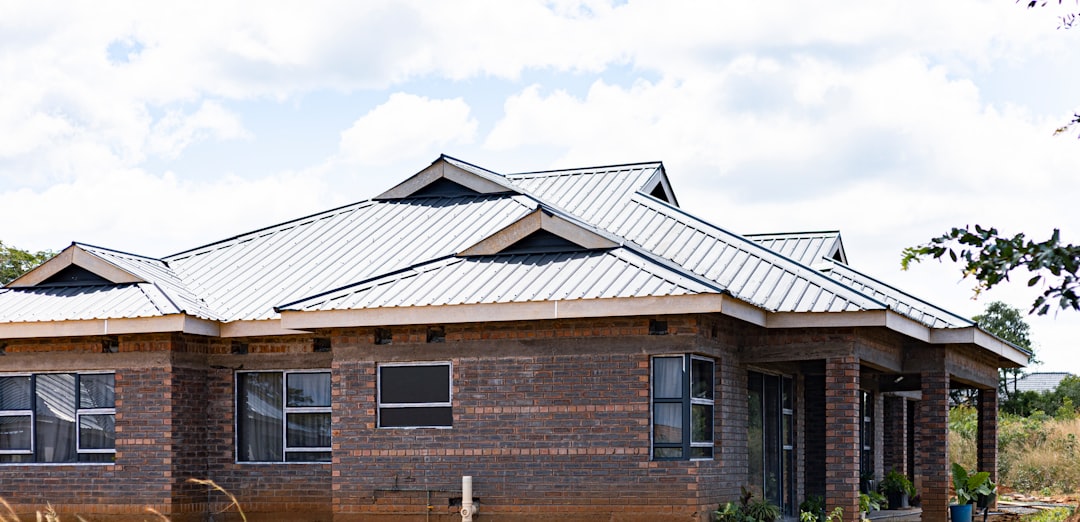 09ac7d6902f648aca6ee501b676fb995 A house with dark brick walls and a light metal roof under a cloudy sky