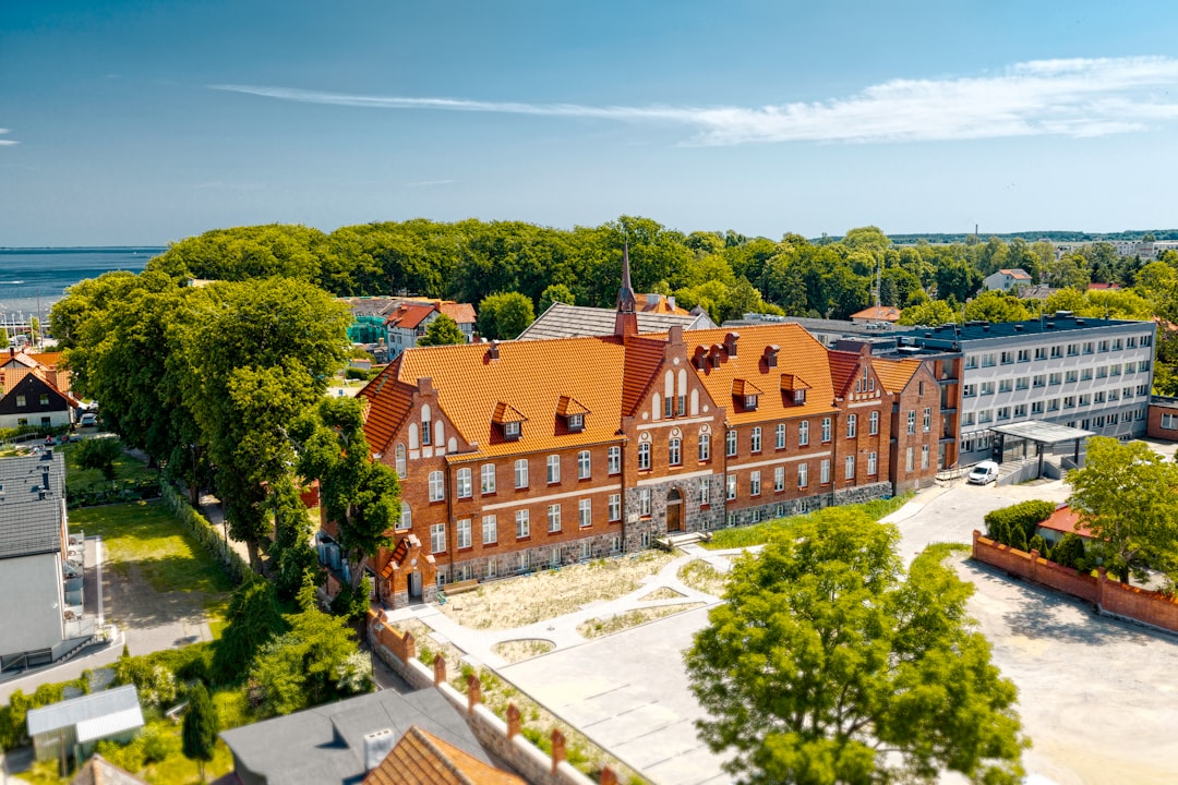 Red-roofed brick building surrounded by green trees near the coast