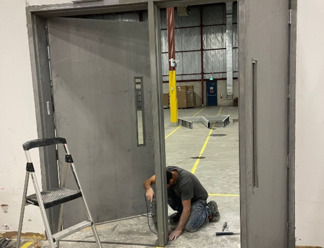 236c6b81da1048a5be09f6659efaed29 A man kneeling down next to a metal door