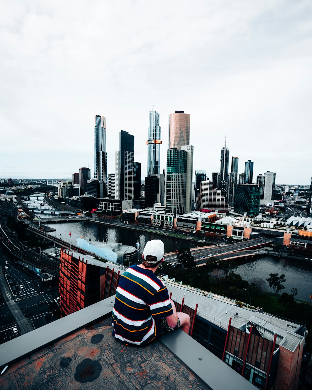 270ef6028ab24bf19ae7c4057d8162d5 man in white red and blue striped shirt sitting on the edge of a building looking