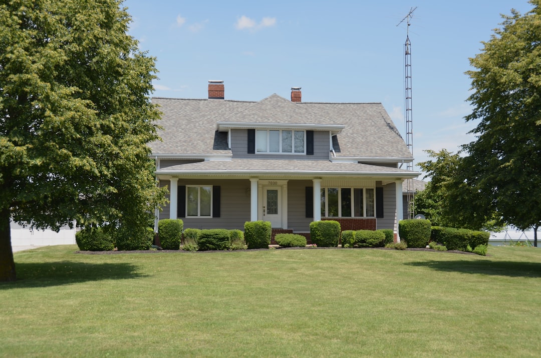 Traditional grey house with a porch, green lawn, and trees