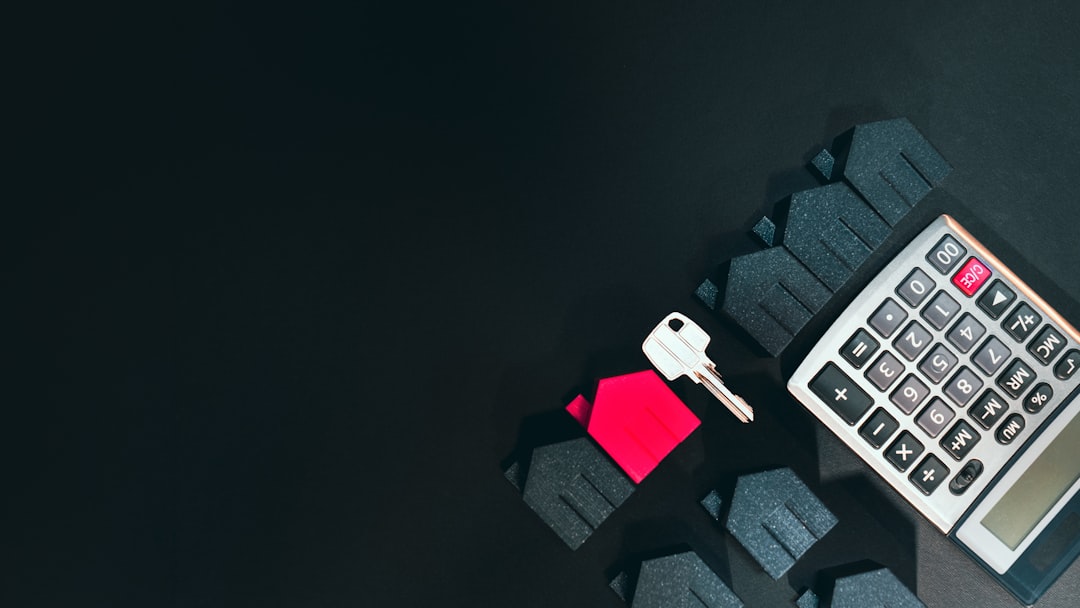 51eeef4a063546089adf95f6296c32b9 A silver key, a red house model, and a calculator on a black surface