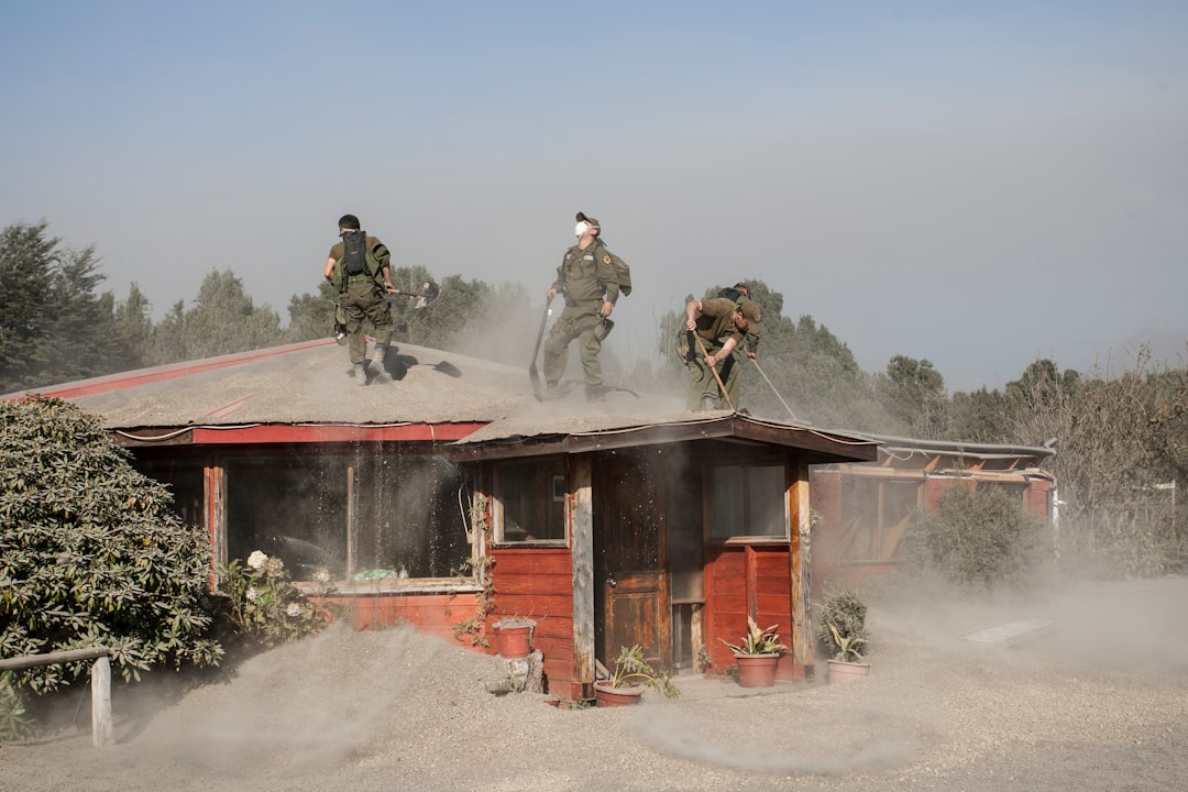 Three people clear volcanic ash from a red house roof