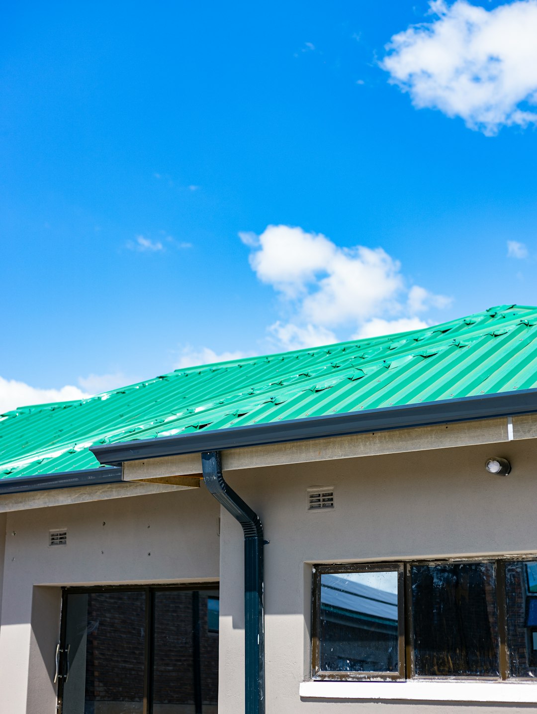 A green corrugated metal roof on a beige building under a blue sky