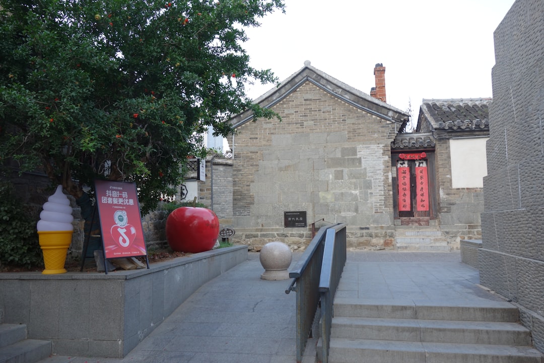 A stone building with a red door beside a large red apple sculpture