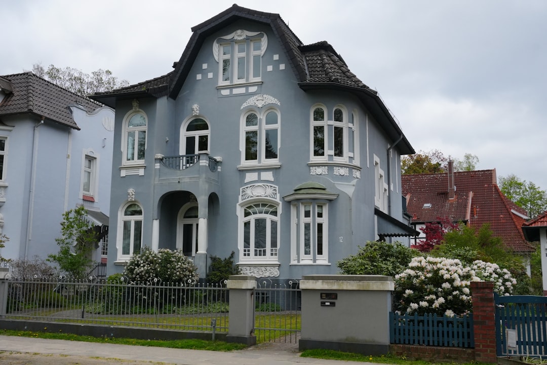 Ornate light blue house with white trim and flowering bushes