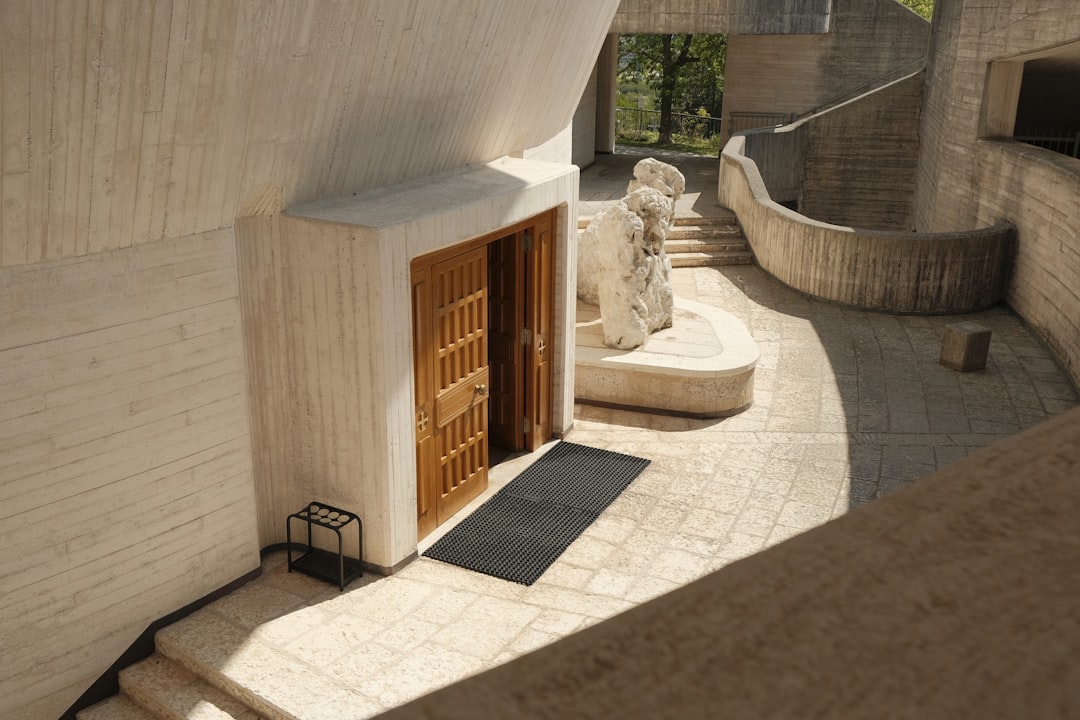 cd4b306776e8416a842fd8e80e73d201 A wooden door in a concrete wall with a black mat on stone steps