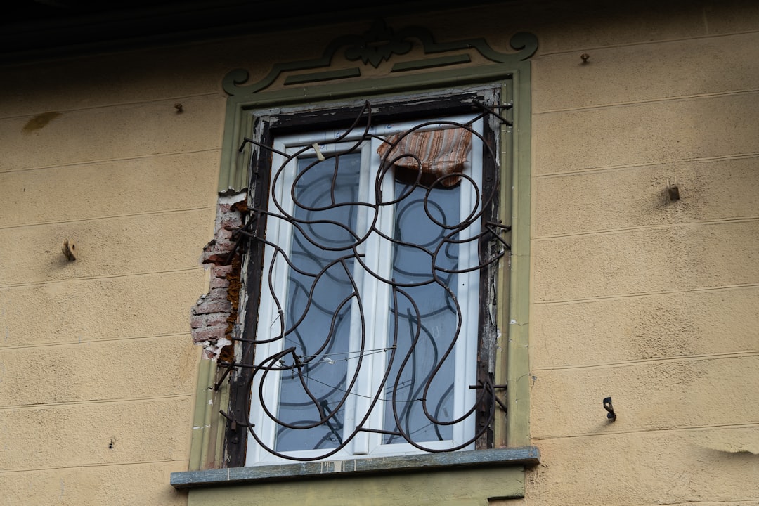 d0c66cb7c2a1429499576506e3b135a8 A weathered window with ornate iron bars and peeling paint